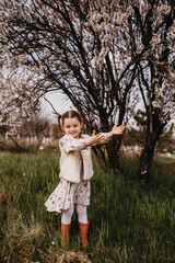 Little girl standing in a garden under a cherry tree in bloom, catching petals.