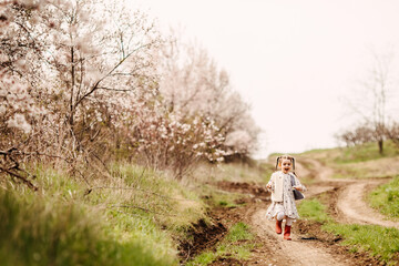 Naklejka na ściany i meble Little girl in rubber boots running on a path in countryside on spring day.