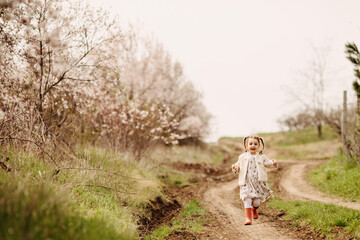 Naklejka na ściany i meble Little girl in rubber boots with two braids, running on a path in countryside on spring day.