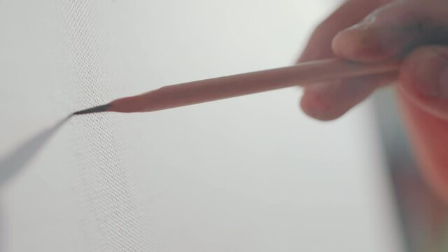 Close up shot of hand of artist drawing with sharp pencil on canvas while working on new picture