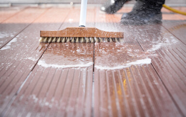 Detail of a man with a scrubbing brush and a water hose making spring cleaning of a wooden terrace floor