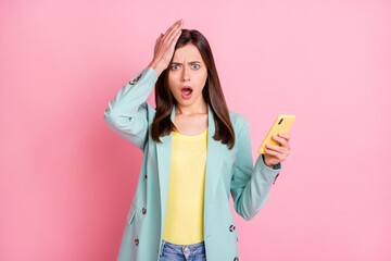 Photo portrait of upset girl touching head holding phone in one hand isolated on pastel pink colored background