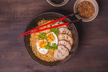 Ramen Soup with chicken in Bowl on wooden table. Beef ramen served Asian style. Raw egg cooks in steaming hot savory broth.