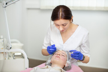 A female doctor cosmetologist dermatologist applying face mask on young woman face making professional skin care and treatment in the cosmetology office. Acne and skin problems
