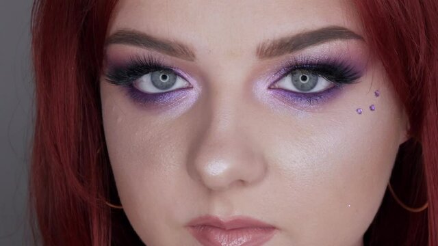 Close-up view of beautiful young girl model with bright red hair and purple makeup posing in the studio