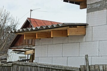 a row of brown wooden planks of formwork under a gray slate roof on a white brick wall