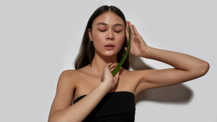 Fototapeta premium Young asian woman with closed eyes holding aloe leaf