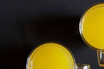 Glass mugs filled with orange or pineapple juice, or mango juice are placed on a dark surface. View from above. Free space for an inscription