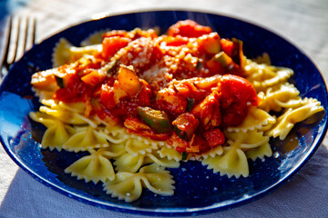 Farfalle shaped pasta on blue plate with homemade fresh vegetable sauce for dinner
