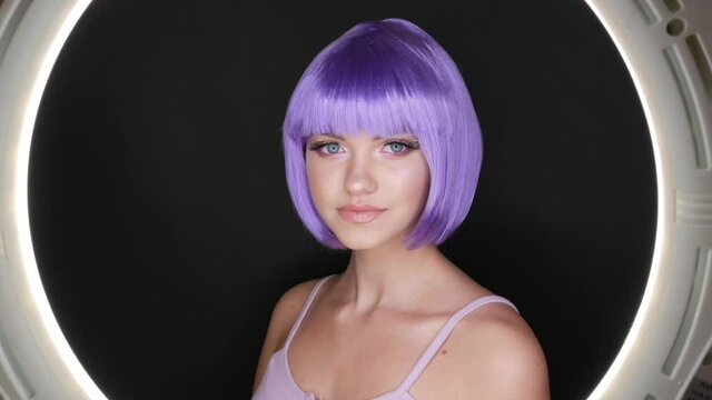 Beautiful young girl model posing in a purple short bob wig, rhinestones on her eyes and stylish pink makeup, high fashion
