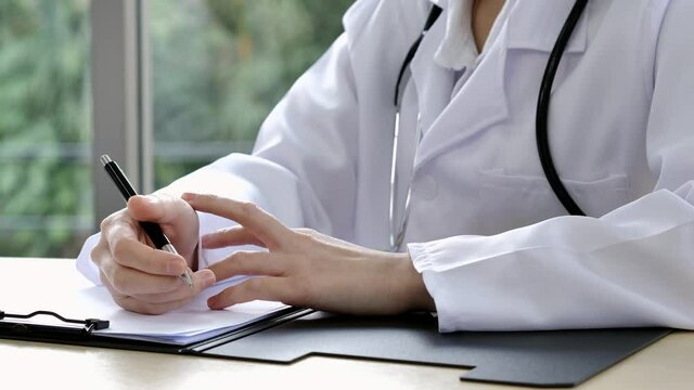 A close-up of the hand of a female doctor or nurse is holding a pen and using another hand to explain information or something with a blurred background.