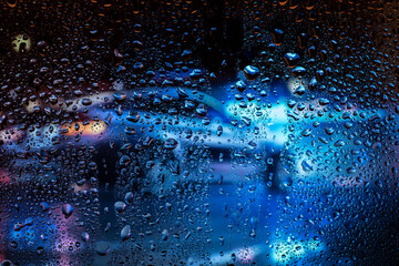 Night city life through windshield. Cars, lights and rain, vintage style photography. City view through a window on a rainy night. Waterdrops on window with road light bokeh.