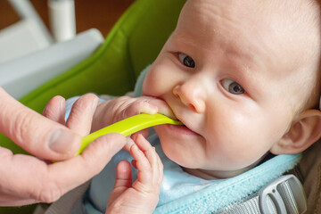 Father feeding cute little baby boy with first solid food. Baby with the spoon in his mouth