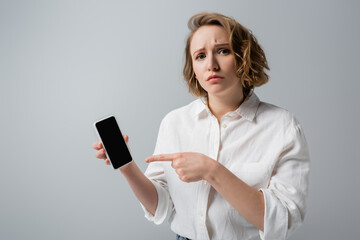 Fototapeta premium young overweight woman pointing at smartphone with blank screen isolated on grey