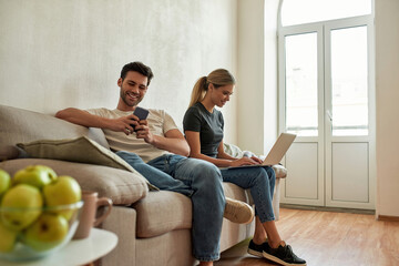 Young couple sitting on couch and surfing the net