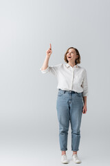 full length of happy overweight woman in jeans pointing with finger on grey