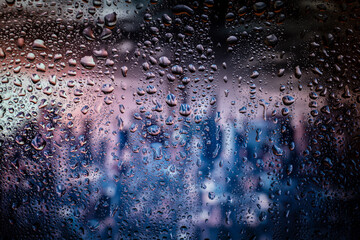 Raindrop on the window, backgorund is bluried a light of city. City life in night in rainy season abstract background.