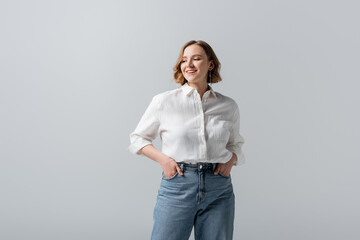 smiling overweight young woman in jeans posing with hands in pockets isolated on grey - Powered by Adobe