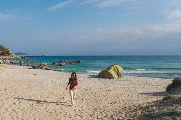 Woman walking on the beach with camping tent.