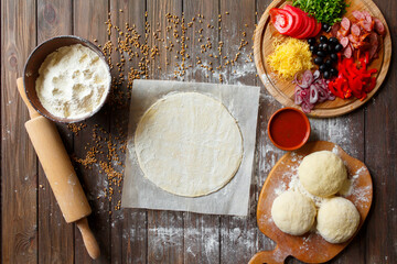 Pizza dough with ingredients on wood table