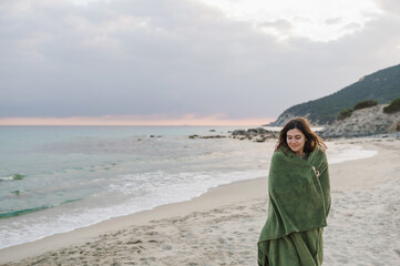 Young attractive woman walking on the beach shore wearing a blanket.