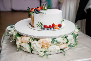 Obraz na płótnie Canvas A beautiful wedding cake decorated with fruits, raspberries, strawberries and blueberries, watered with caramel. Confectionery on the table. Holiday concept.