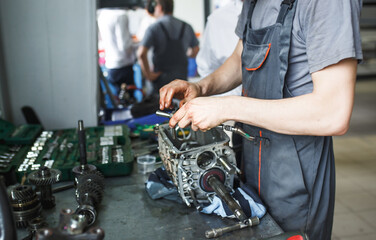 The hand of a car repairman with keys and a special tool on the background of the service area. A mechanic repairs the engine in a car service station in uniform. Copy space