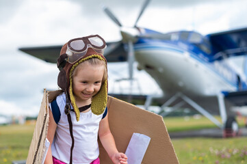 A cute little girl dressed in a cap and glasses of a pilot on the background of an airplane. The...
