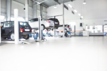 Car repair service in defocus, industrial background. Cars on lifts, transport service area, the mechanic repairs the car. Copy space