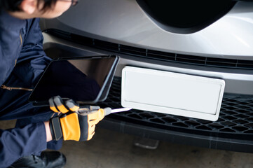 Asian auto mechanic holding digital tablet checking car engine and license plate in auto service...