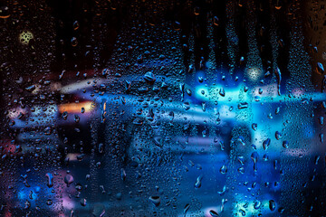 Night city life through windshield. Cars, lights and rain, vintage style photography. City view through a window on a rainy night. Waterdrops on window with road light bokeh.