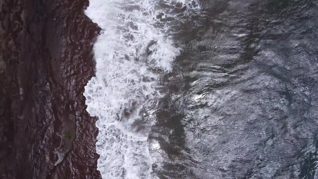 Aerial top view waves break on volcanic rocks in Jeju Island.