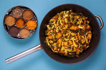 Fried dish with potatoes, cabbage and kale leaves. Indian vegetarian cuisine Subji meal. Masala dabba spice box top view.