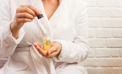 Obraz na płótnie Canvas woman in bathrobe holding dropper bottle serum collagen hyaluronic acid oil natural cosmetics concept