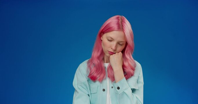 Tired young woman with pink hair waking up from nap on blue background