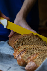 Front view of male hands cutting brown bread with a yellow knife