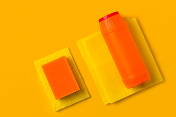 Yellow and orange cleaning sponges and bottles of detergent on a yellow background with copy space. Household chores or house cleaning services. Cleaning products concept