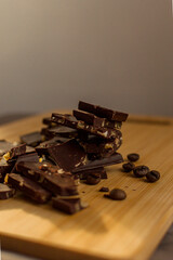 Broken slices of chocolate on a cutting wooden board, coffee grains in the background, texture, copy spase.