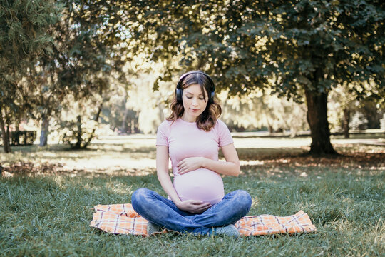 Young pregnant woman listening to music in the park on a spring or summer day. Place for text.