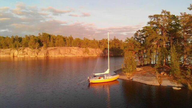 Sailing boat in natural harbour in the Swedish archipelago. Calm and beautiful summer evening at golden hour. Aerial shot dolly out.