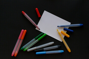 Markers and felt-tip pens in different bright colors, white sheet, black background, top view, copy space.