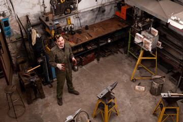 Artisans portrait. Traditional metalworking process in a forge. Blacksmith in the workshop posing, top view.