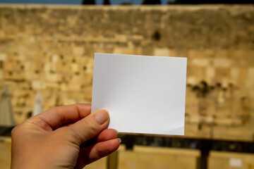 Hand holds a small piece of paper to write a note, against the background of the Wailing Wall (Western wall) in Jerusalem, Israel