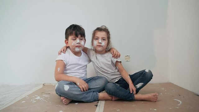 Caucasian kids paint the walls Boy and girl took a break and have fun Children's faces are painted Boy and girl kiss each other Twins make repairs Funny kids Happy family Slow motion