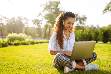 Young woman freelancer sitting on green grass with laptop. Education online. Happy woman with...