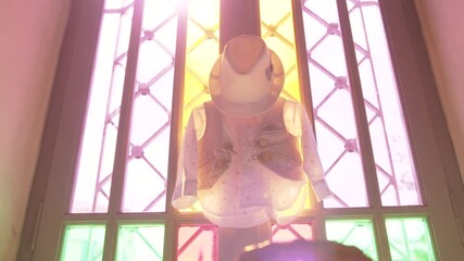 Baby christening dress hanging at front door entrance with sunlight filtering through stained glass
