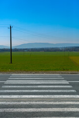 Crosswalk on the countryside road with a green field in the background, safe sidewalk with the pedestrian crossing. View on the field with mountains and crosswalk on the asphalt.