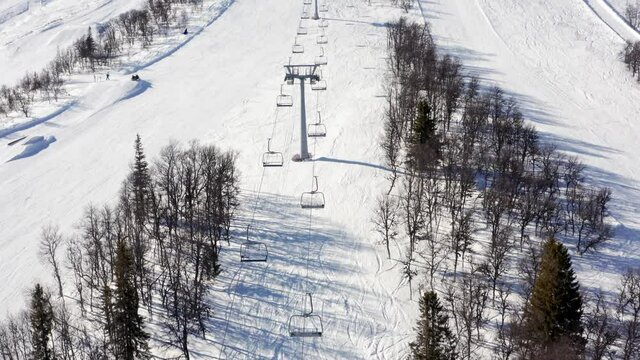 Empty skiing chair lift in closed ski resort due to corona virus in beautiful sunny winter snow season. Alpine mountains aerial drone view