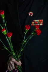 the hands of an old war veteran hold flowers. red carnations as a gift for a military holiday in honor of the winners of the Second World War. patriotic holiday victory day. congratulations to old man