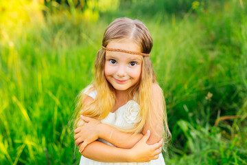 Naklejka na ściany i meble Smiling girl on a green meadow, a small child hugs herself, wear